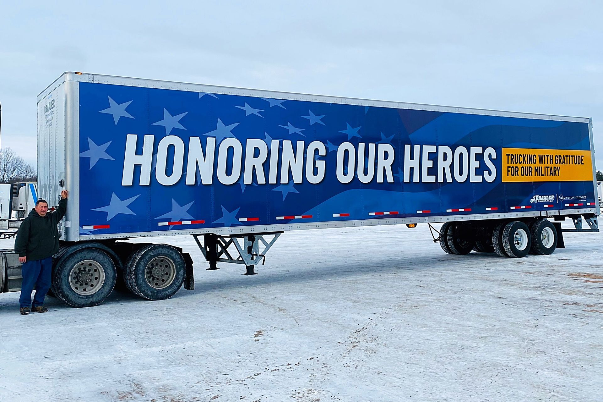 A person stands beside a semi-trailer featuring a blue banner with stars and the text 