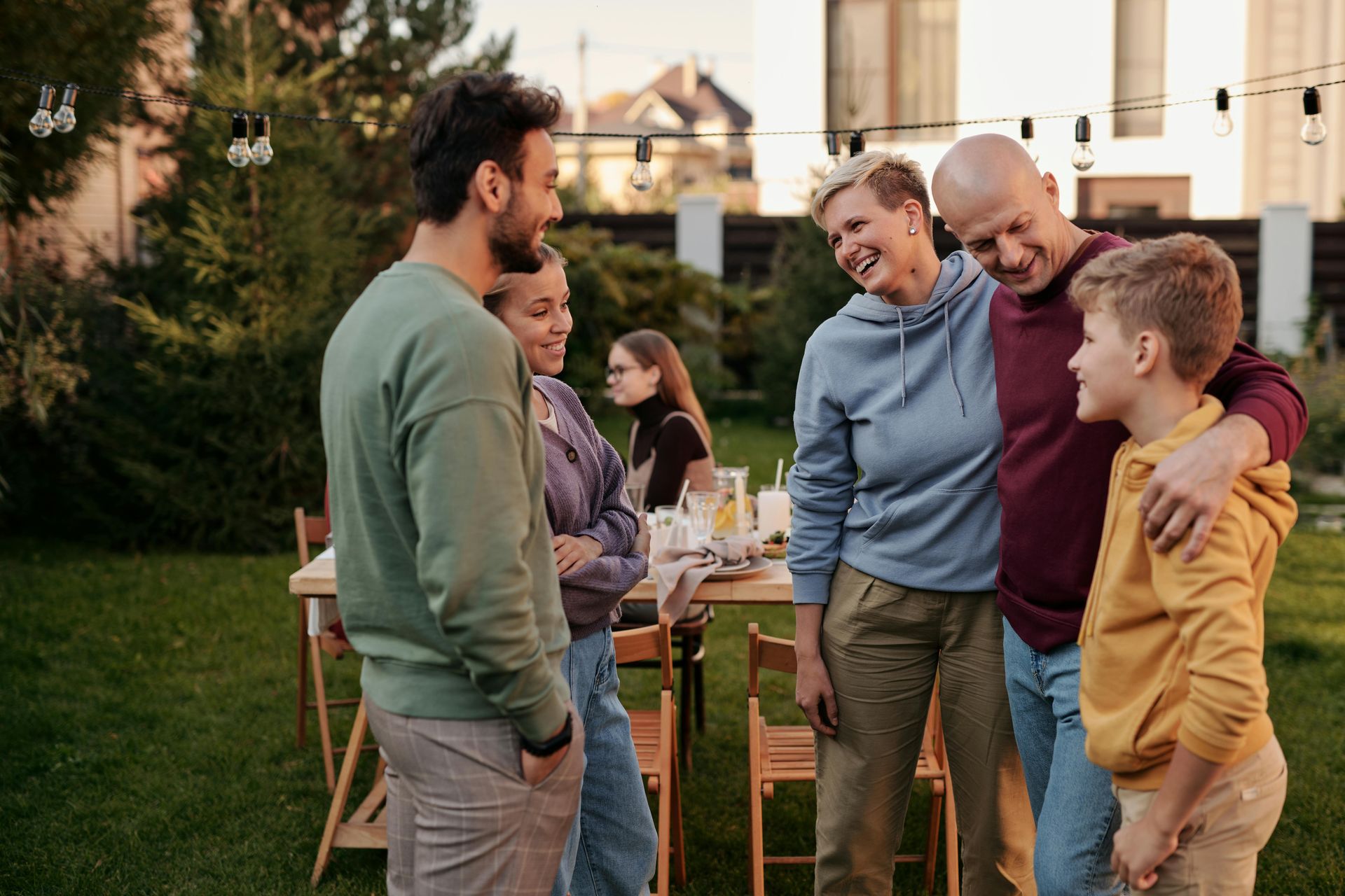 A group of people talking and laughing together during an outdoor gathering in a backyard at sunset.