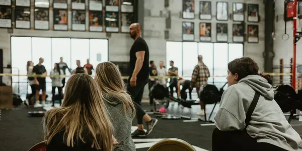 People watch a weightlifting competition in a gym, focusing on the athlete in the center.