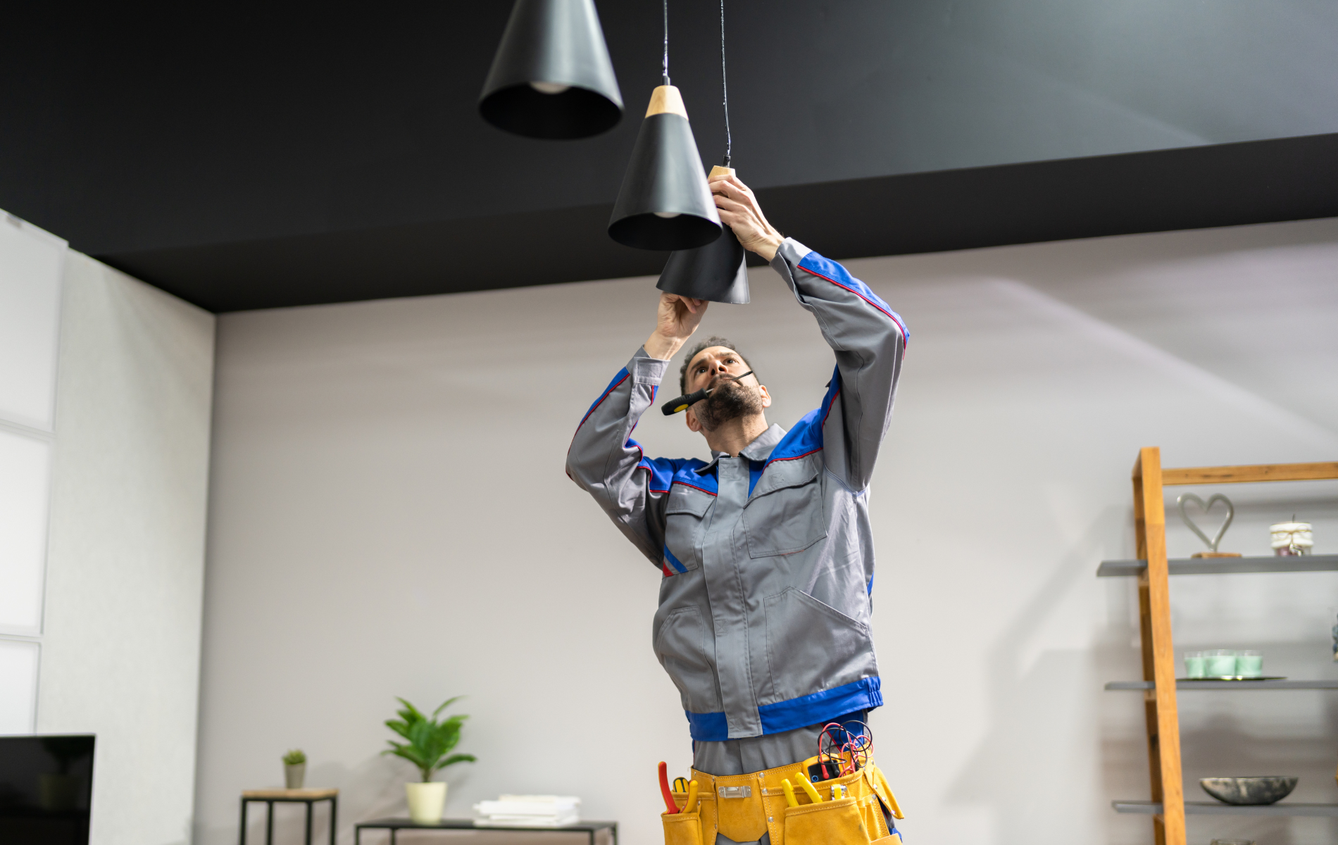 Electrician in gray uniform installing black pendant lights in a home.