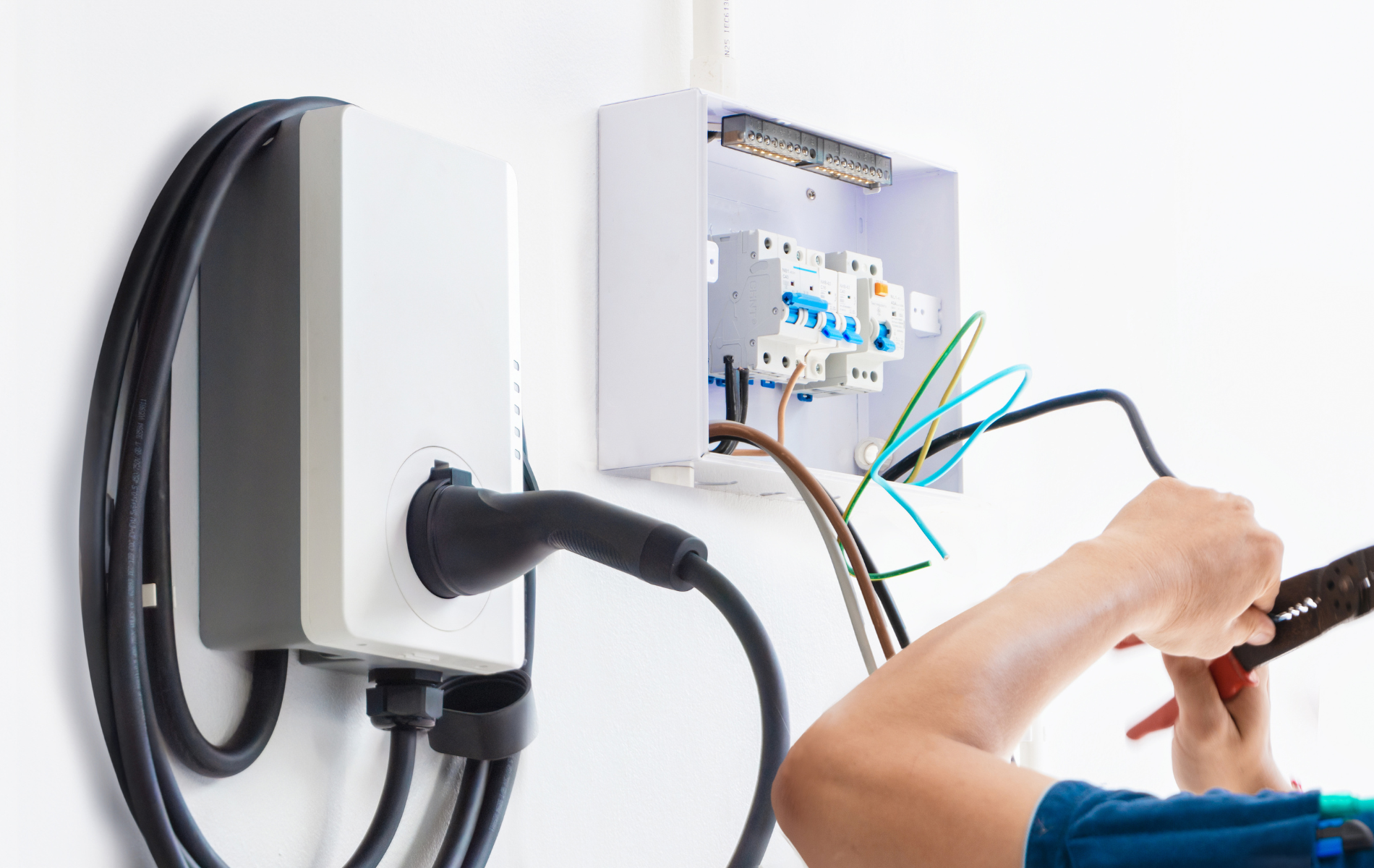 Electrician installing EV charger; wiring to a breaker box, white wall.