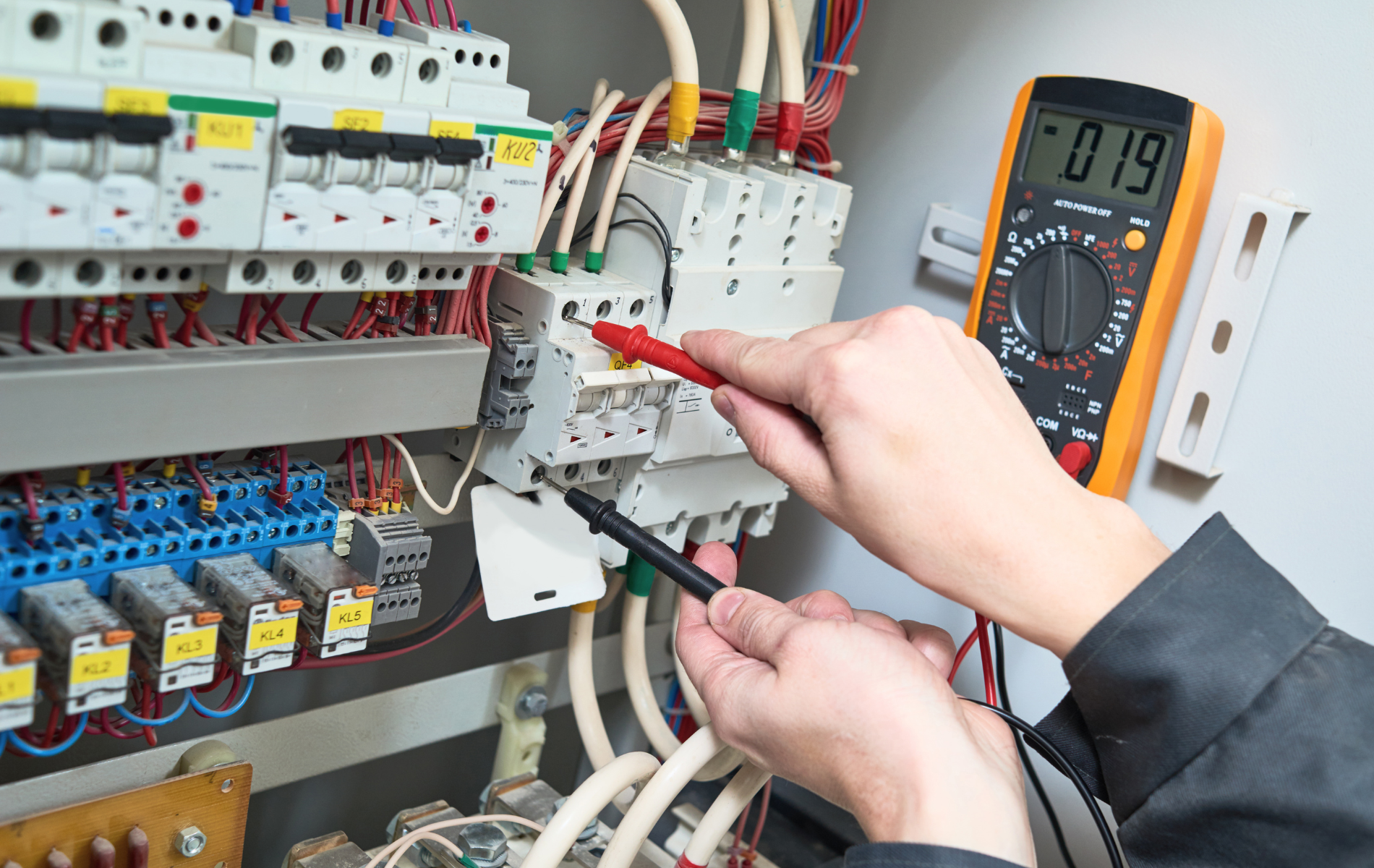 Electrician using a multimeter to test wires in a circuit panel.