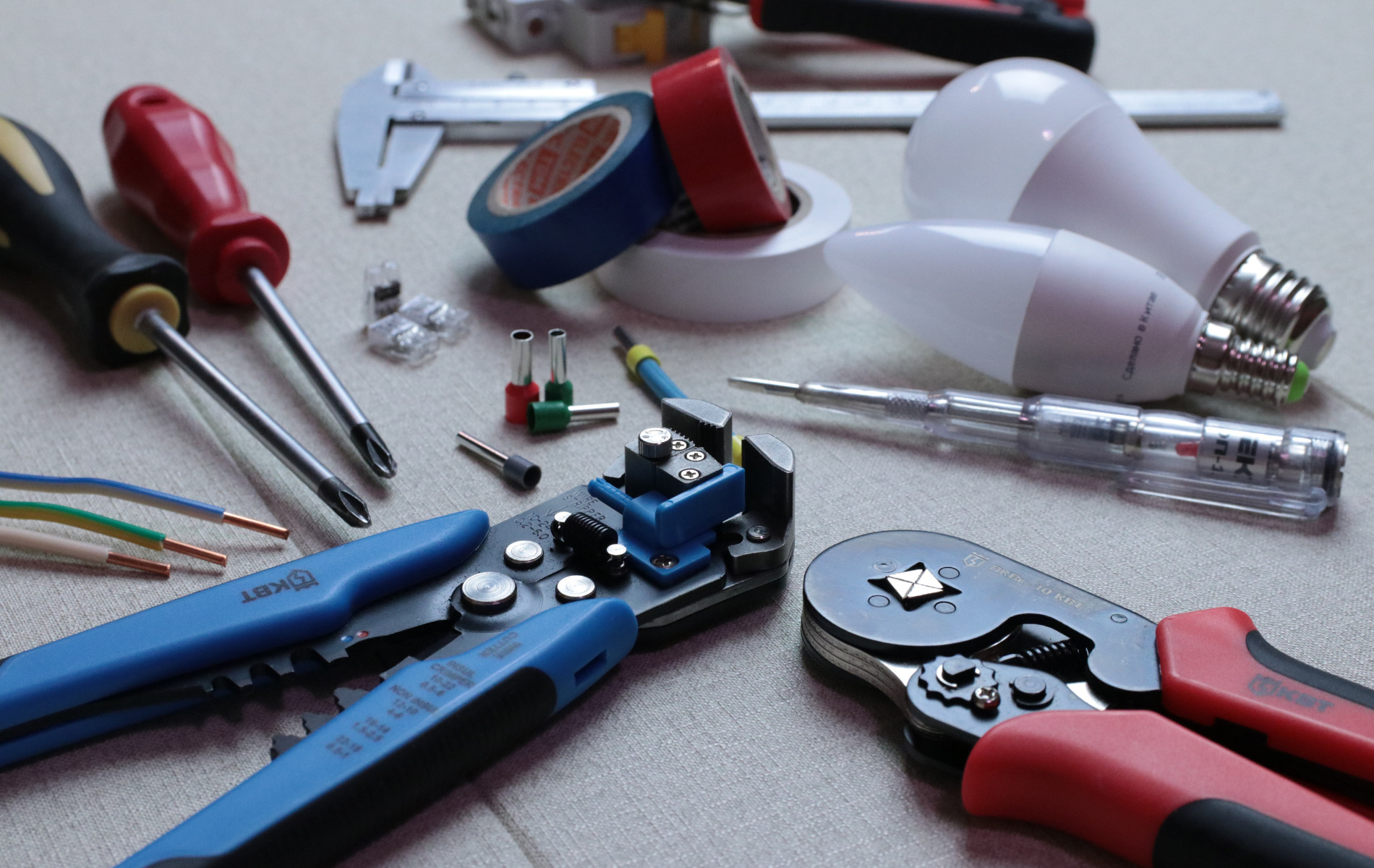 Tools of an electrician laid out: screwdrivers, wire strippers, wire connectors, light bulbs, tape