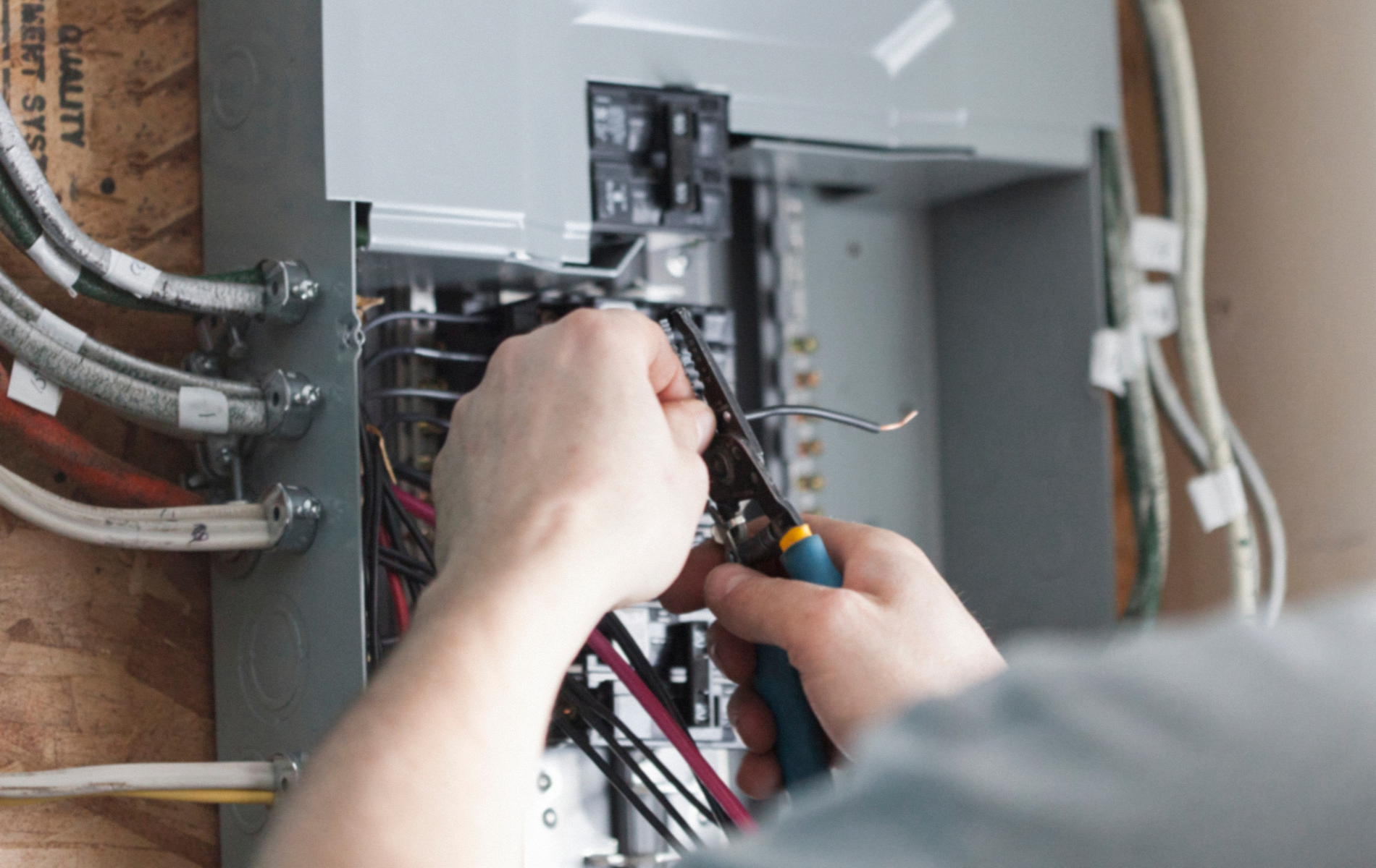 A person working on electrical wiring in a breaker box, using pliers.
