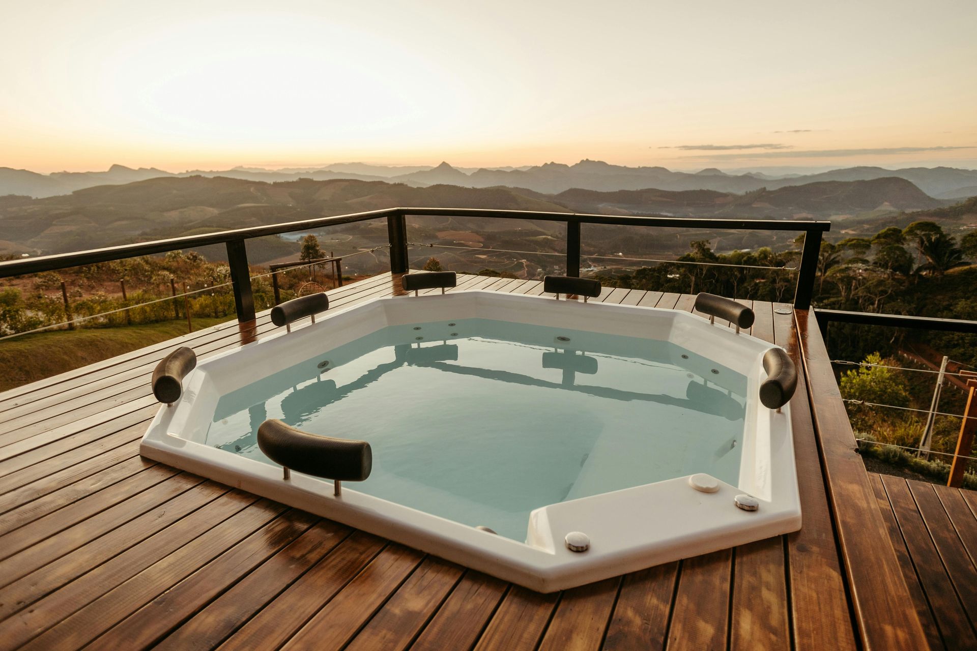 Hot tub on wooden deck overlooking mountain vista at sunset.
