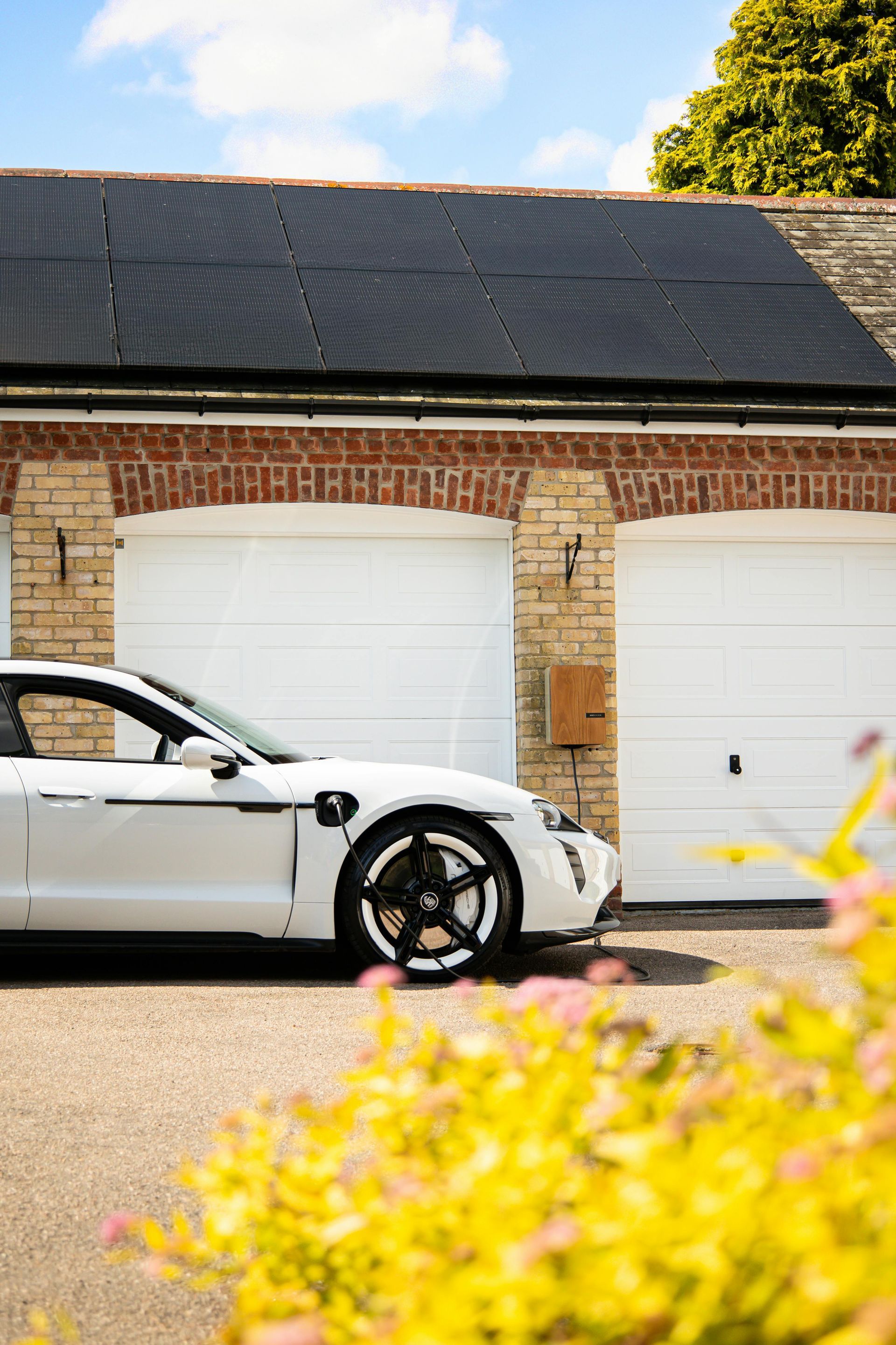 White electric car parked in front of a brick garage with solar panels on the roof.