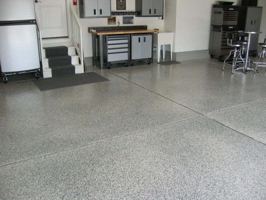 Garage with gray speckled epoxy floor, storage cabinets, workbench, and stairs leading up.
