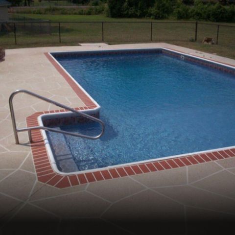 Rectangular swimming pool with brick trim and a gray stone patio. Handrail leads into shallow end.