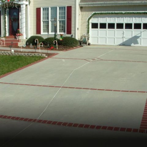 Concrete driveway with red brick border, leading to a house with white garage and Christmas decorations.
