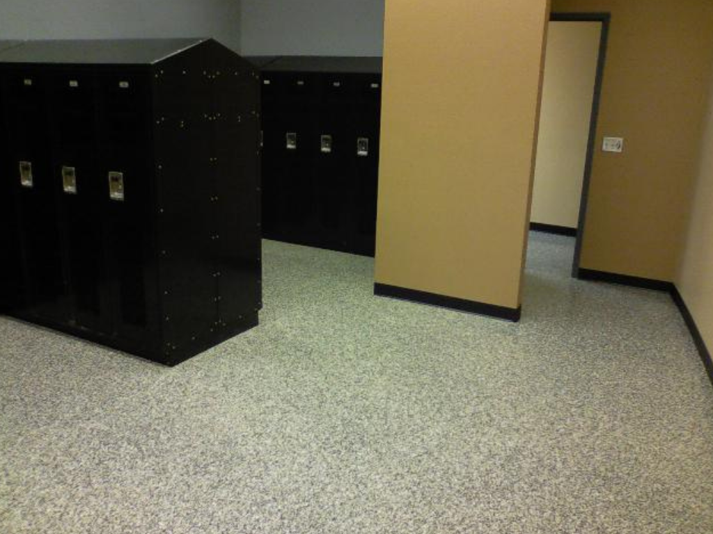Black lockers in a room with speckled gray flooring, beige walls, and an open doorway.
