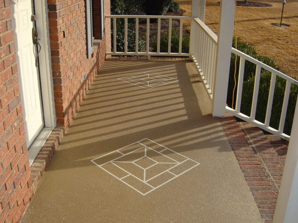 Beige porch with white railing, brick exterior, and decorative concrete design on the floor.