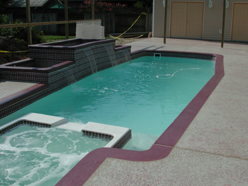 Swimming pool with cascading waterfall, attached spa, and burgundy tile accents.