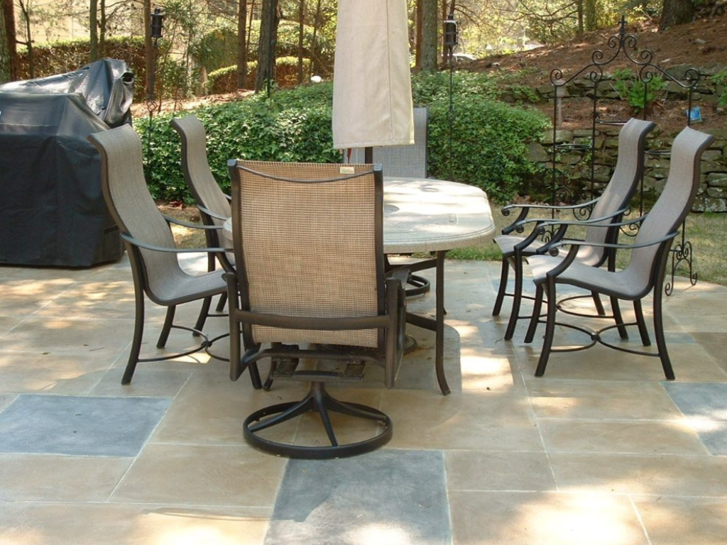 Patio set with table and chairs on a stone patio, umbrella, and grill in a backyard setting.