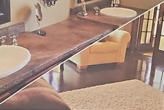 Bathroom with dark countertop, two sinks, and a tan armchair.