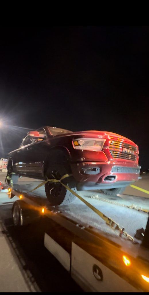 A red car is being towed by a tow truck at night.