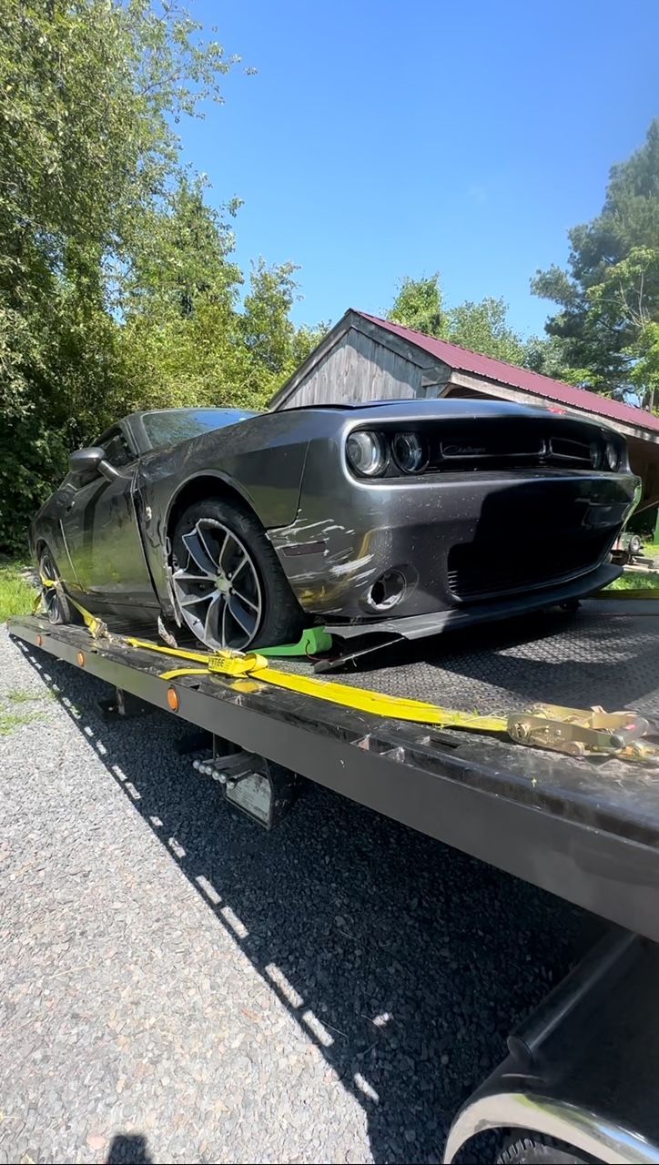 A gray dodge challenger is sitting on top of a tow truck.