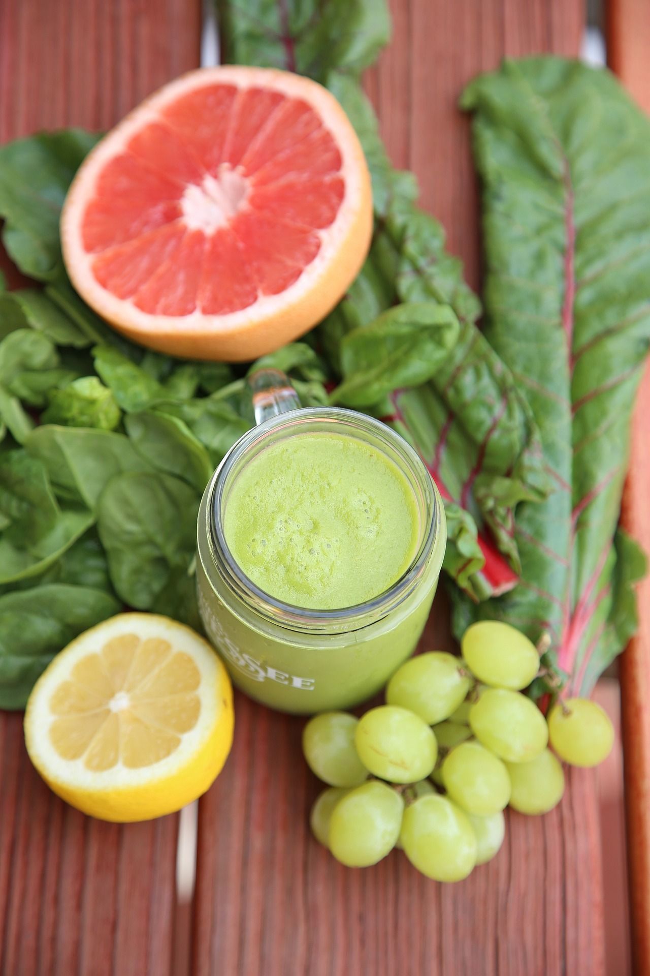 A green smoothie in a jar surrounded by grapes , lemons , spinach and grapefruit