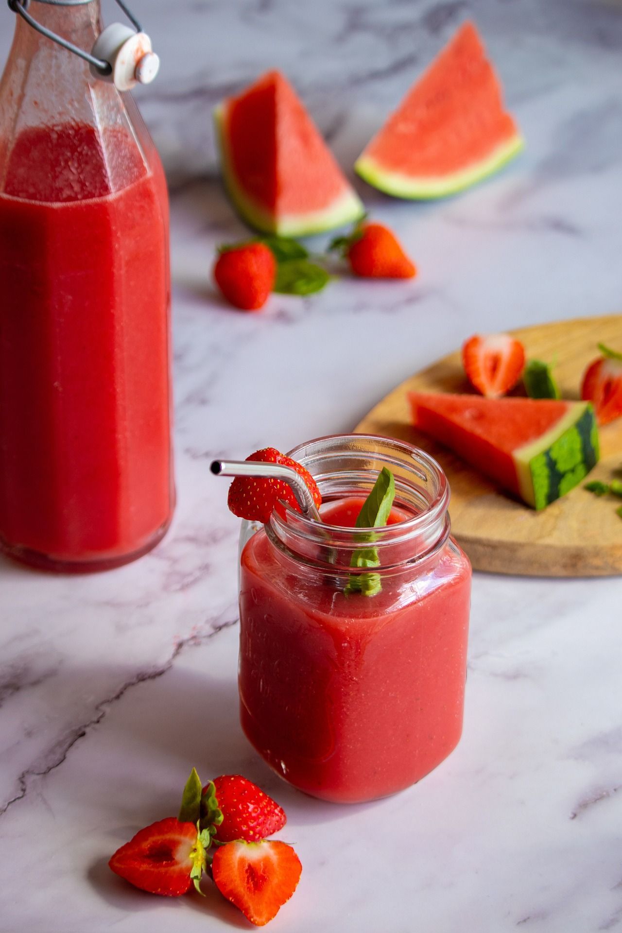 A watermelon and strawberry smoothie in a jar with straws on a table