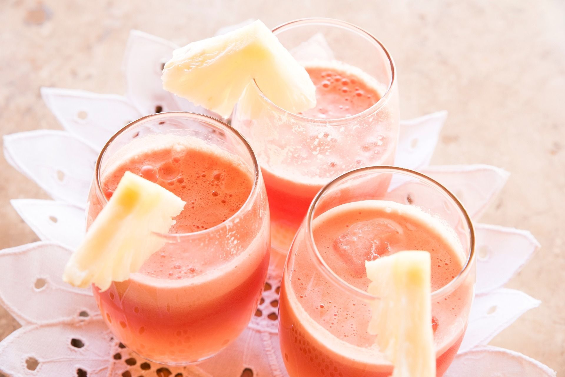 Three glasses of watermelon juice with pineapple slices in them