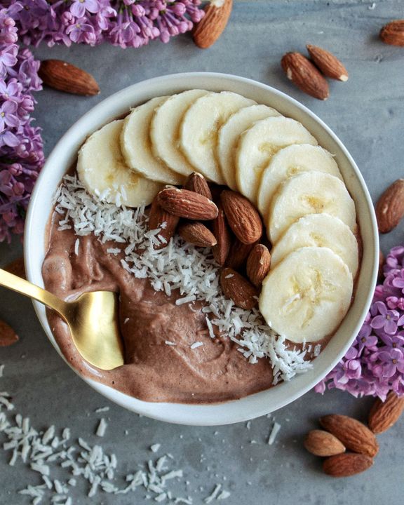 A bowl of food with bananas almonds and coconut with a spoon in it