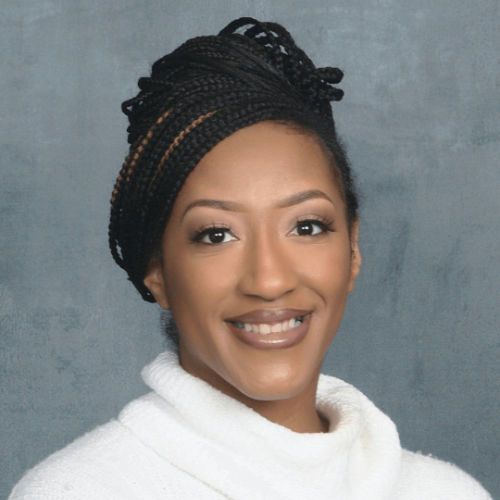 A woman with braids and a white sweater smiles for the camera