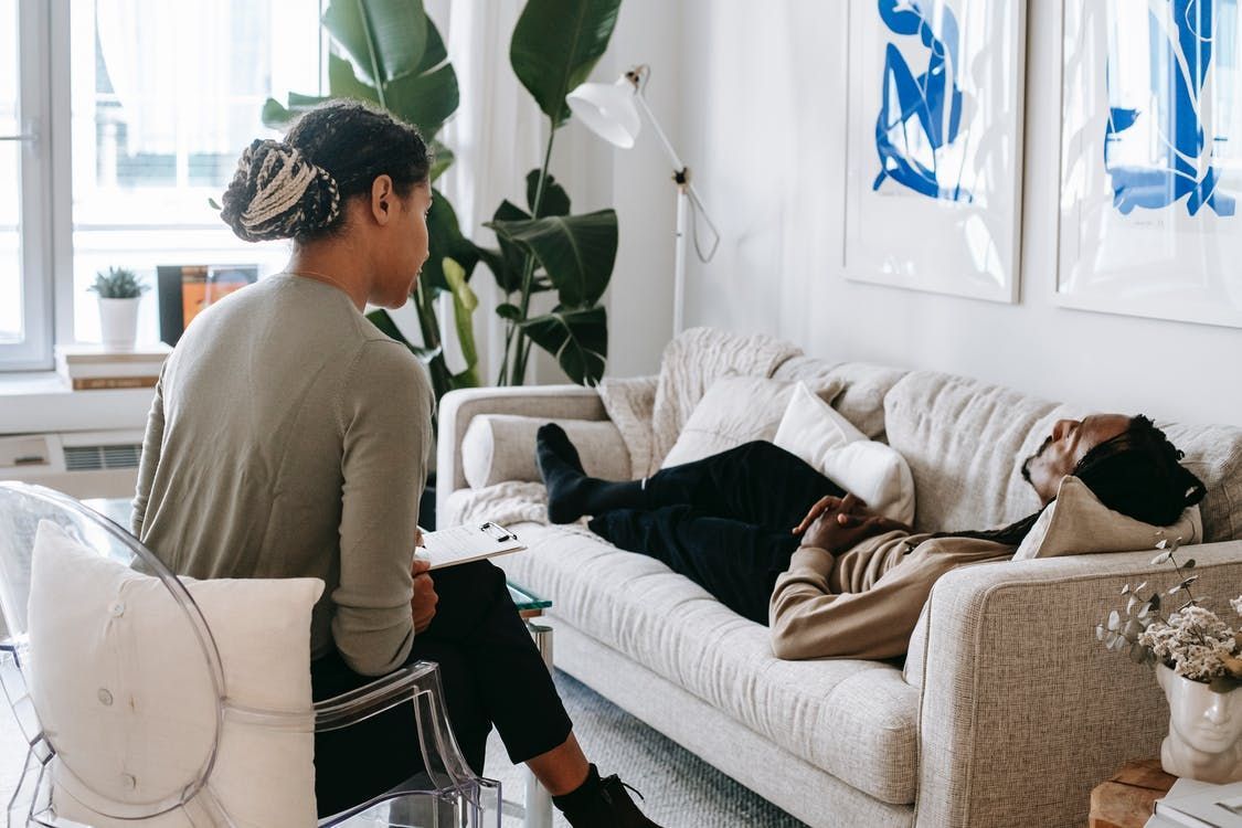 Therapist and patient in a counseling session; patient reclining on a couch, therapist sitting nearby.