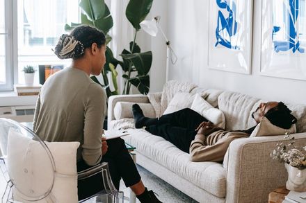 Woman in beige yoga outfit meditates on a mat, eyes closed, arms outstretched, indoors.