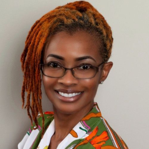 A woman with dreadlocks and glasses smiles for the camera