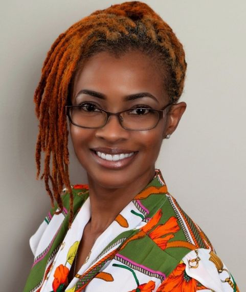 A woman with dreadlocks and glasses smiles for the camera