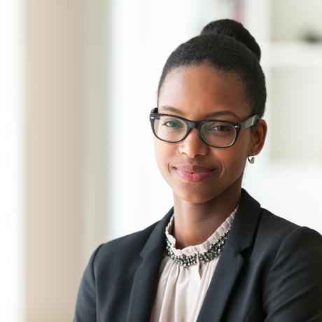 Woman in glasses and a blazer, smiling at the camera.