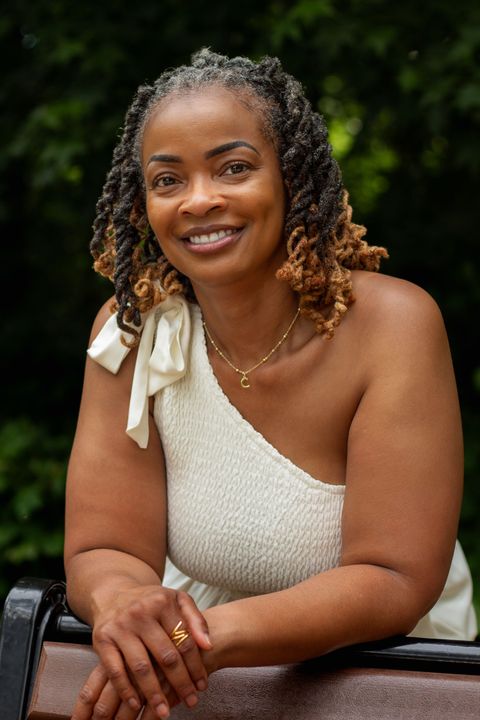 A black woman with locs and glasses smiles for the camera