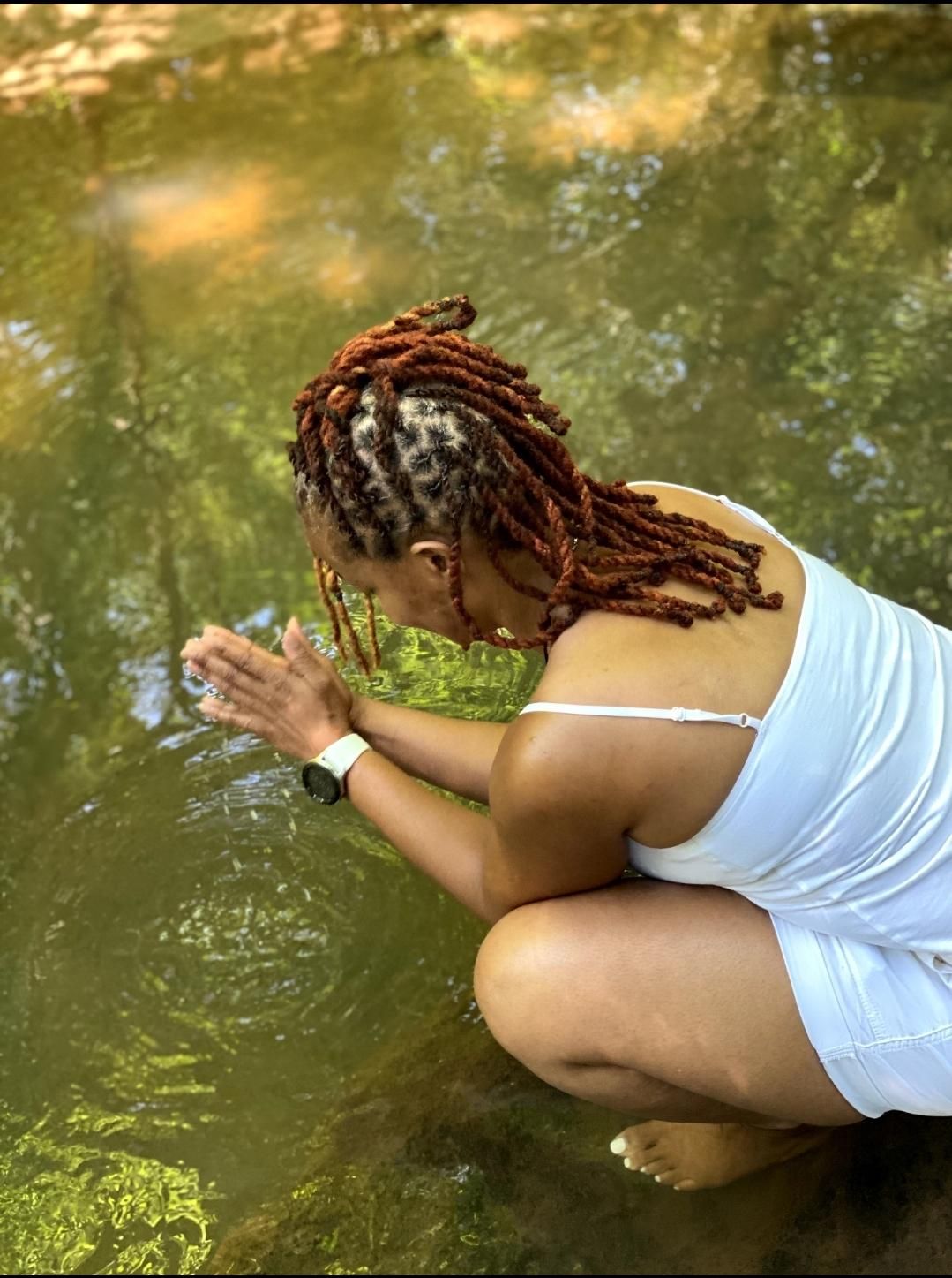 A woman with dreadlocks is kneeling in the water.