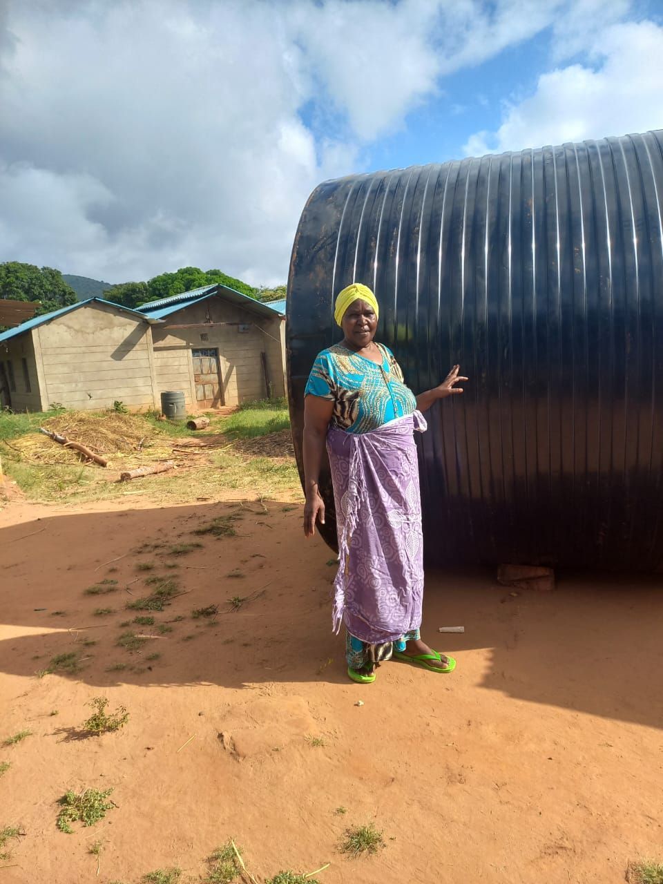 Kenyan woman stands next to her rainwater catchment tank.