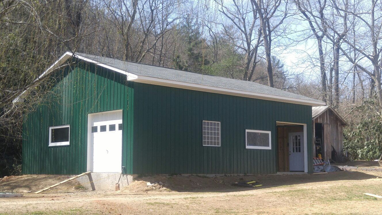 Green metal garage with a white garage door and small windows, in a grassy area with trees.