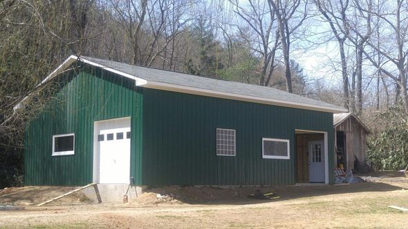 Green metal garage with a white garage door and small windows, in a grassy area with trees.