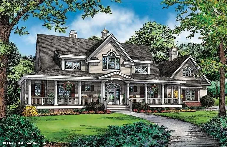 A large, light beige house with a wrap-around porch, surrounded by green lawn and trees.