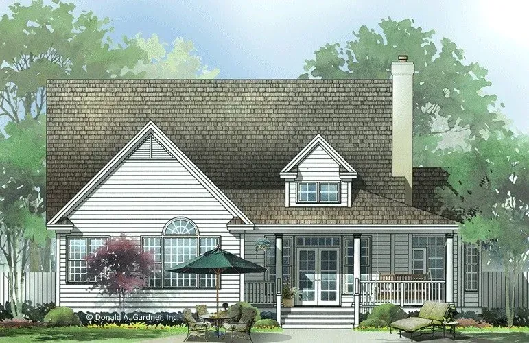 White house with porch, gable roof, and chimney, surrounded by trees and a small lawn with patio furniture.