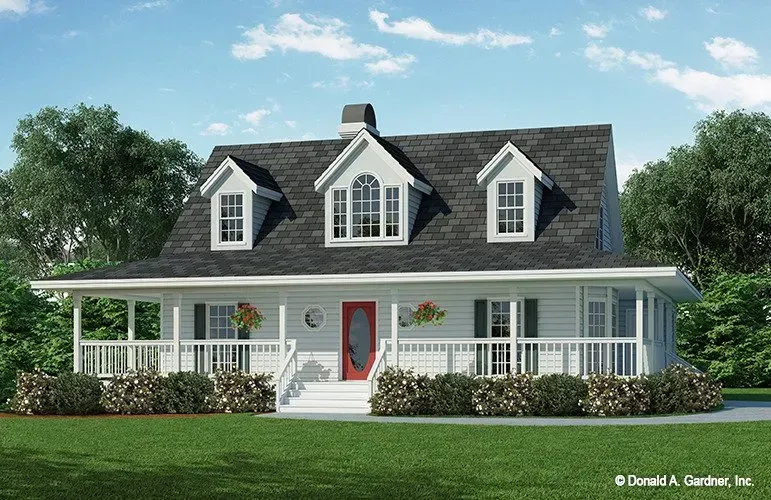 White farmhouse with porch, red door, dormers, and green lawn under a blue sky.