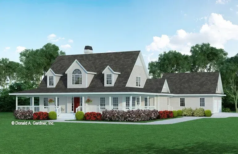 Farmhouse with a wide porch, red door, and dormer windows, set on a green lawn.