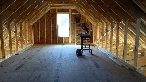 Unfinished attic space with wooden framing, plywood floor, and a window.
