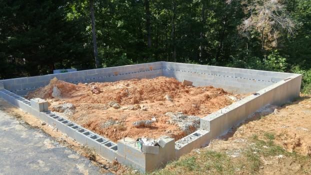 Concrete foundation walls with a dirt-filled interior, likely for a building, in a natural outdoor setting.