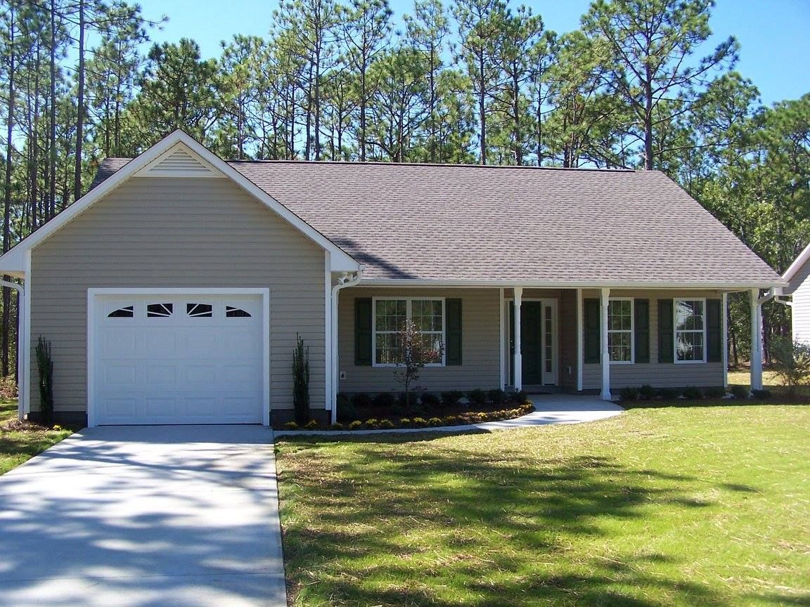 Tan one-story house with a white garage door, porch, and a driveway on a sunny day.