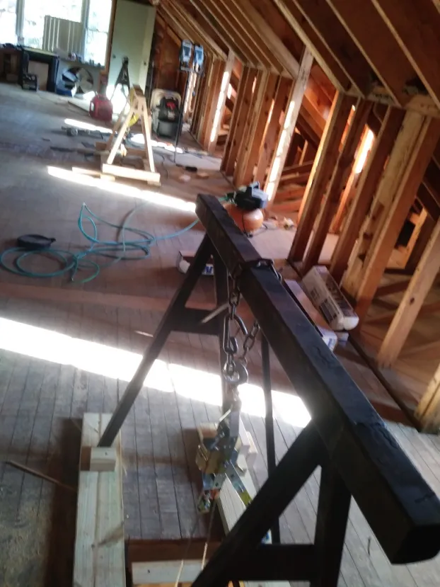 Interior view of a partially constructed attic. Wooden beams and a black structure with hanging chains.