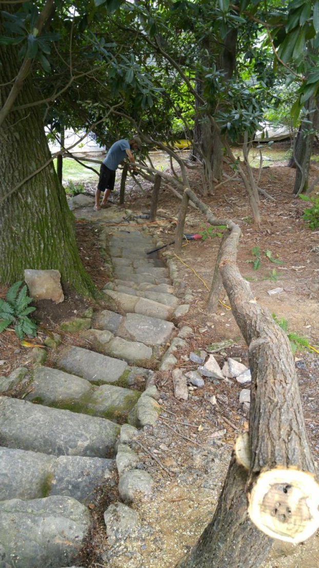 Stone steps with a wooden railing leading up a hillside. A person stands at the top.