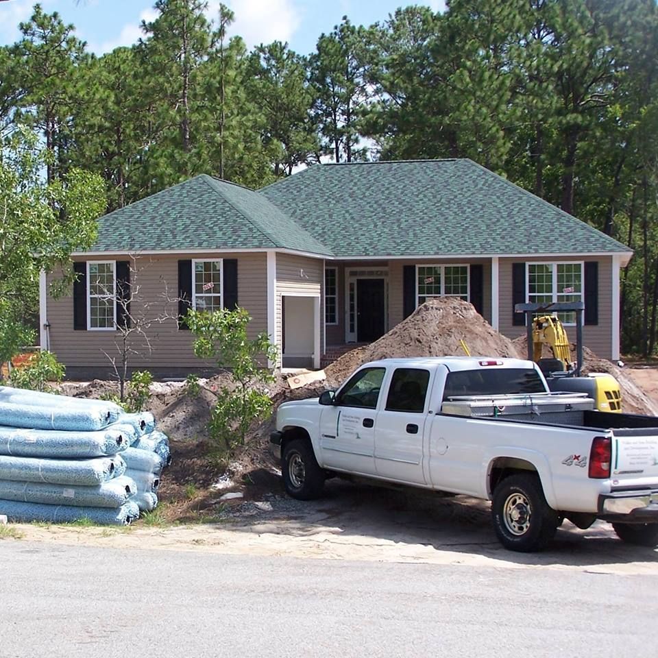 Beige house under construction, white truck parked out front, with a pile of dirt and equipment.