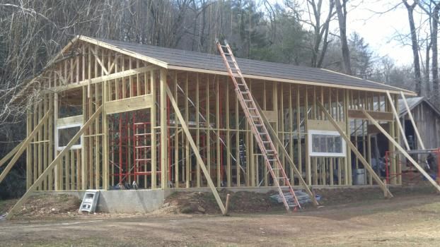 Framed wooden building under construction with a ladder and support beams, outdoors.