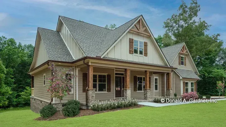 Tan craftsman-style house with brown shutters, front porch, and dormers on a green lawn.