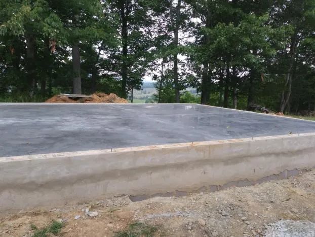 Concrete foundation with low walls, surrounded by dirt and trees.