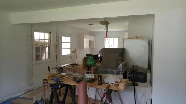 Interior room under renovation, open doorway, work table with tools, white walls, and bright lighting.