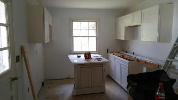 Kitchen under renovation with white cabinets, island, window, and door.